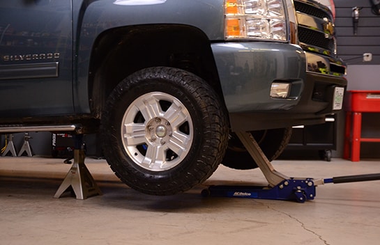 Chris using a floor jack and jack stands to support the front end of the Chevy Silverado 1500